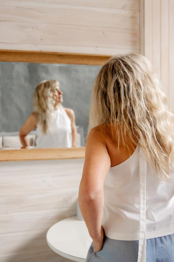 Real woman looking at herself in the mirror while trying on VOUS In her home environment.